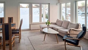 A modern living room with a sofa, coffee table, and chairs, large windows with a view of a snowy landscape. - 5 Star Holiday Home in Falkenberg (Falkenberg)