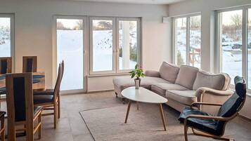 Una sala de estar moderna con sofá, mesa de centro y sillas, ventanas amplias con vistas a un paisaje nevado.