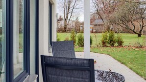 An outdoor patio with two chairs and a table, overlooking a grassy area with trees and a building in the background. - 5 Star Holiday Home in Falkenberg (Falkenberg)