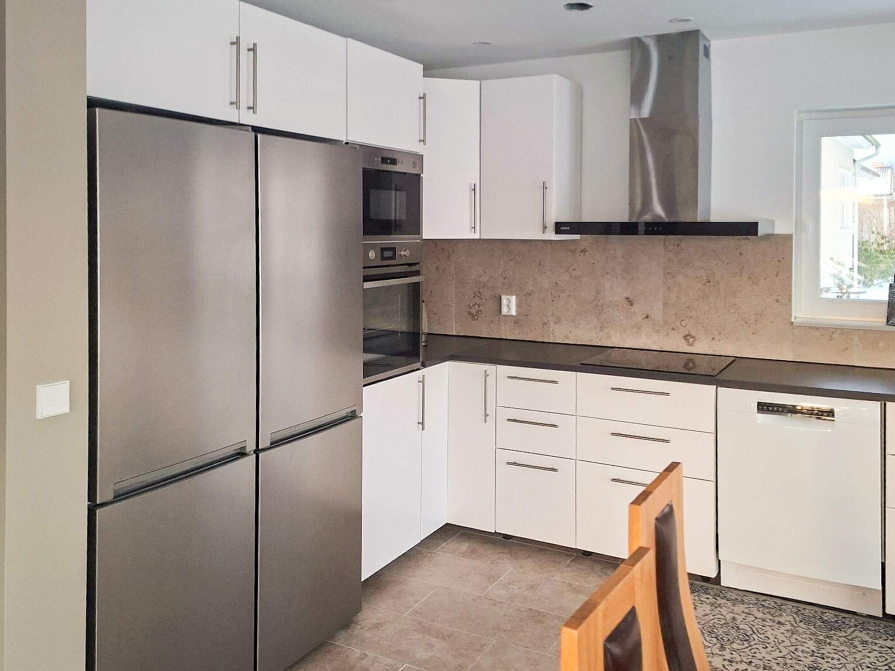 Una cocina con electrodomésticos de acero inoxidable, armarios blancos y un ventanal que proporciona luz natural.