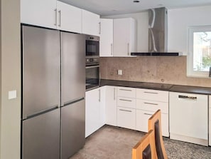 A kitchen with stainless steel appliances, white cabinetry, and a window providing natural light. - 5 Star Holiday Home in Falkenberg (Falkenberg)