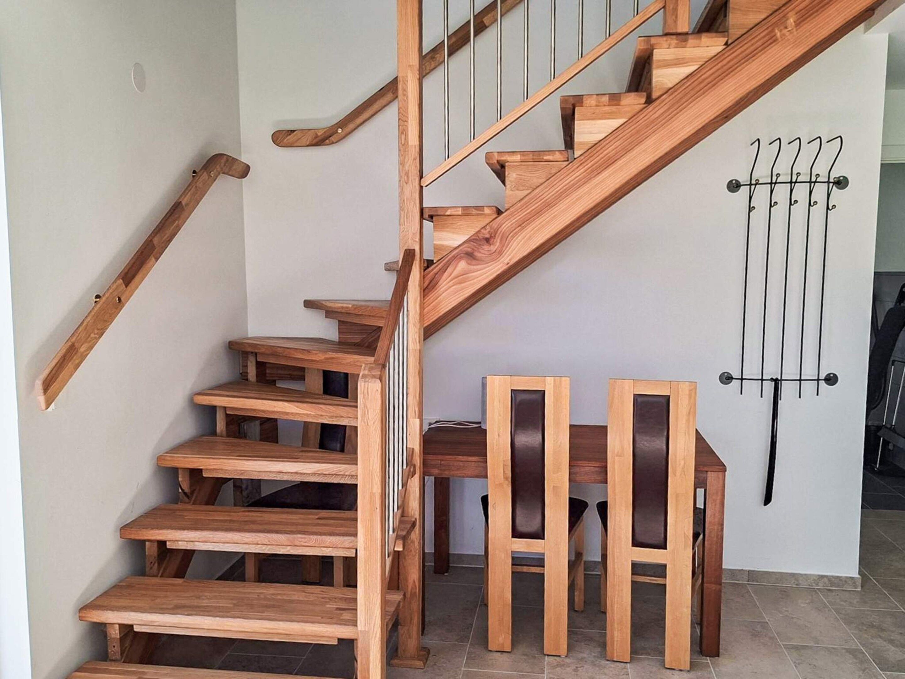 Una escalera de madera con barandilla, un radiador fijado a la pared y dos sillas de madera.