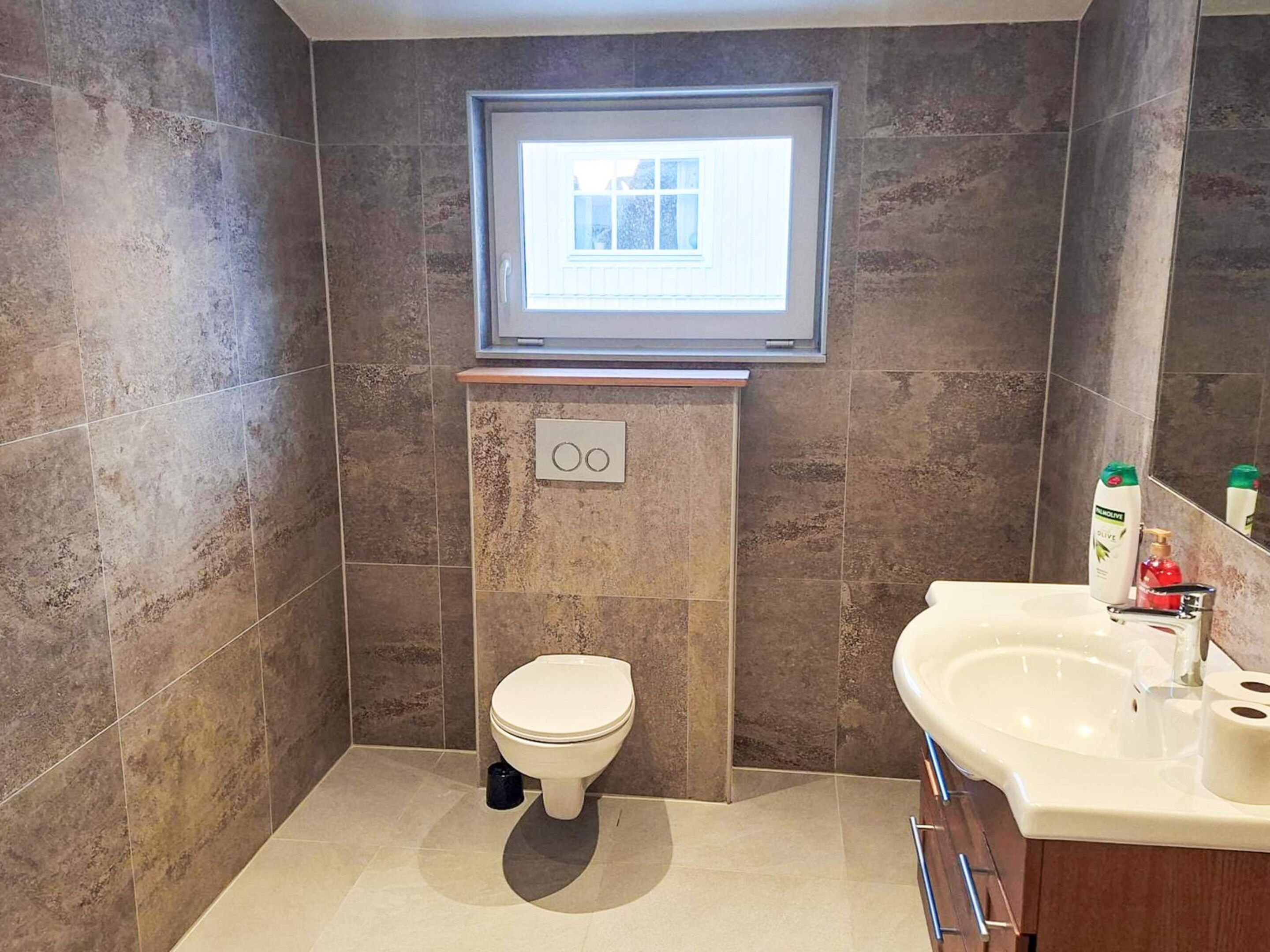 A modern bathroom with a toilet, a sink, and a window above the toilet.