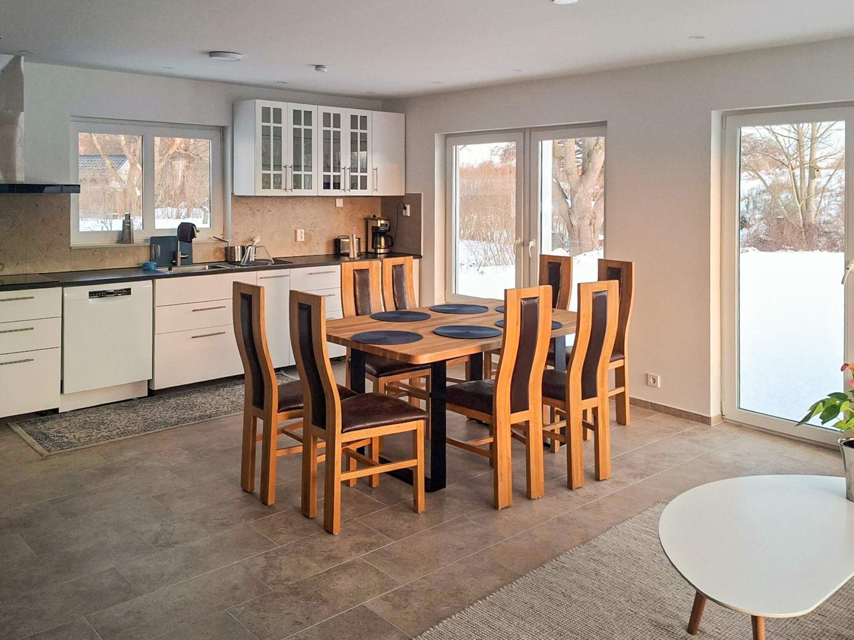 Una cocina moderna con comedor, que cuenta con una mesa grande con sillas, horno empotrado y ventana con vistas al exterior.
