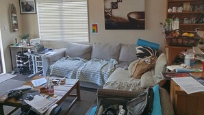 A living room with a sofa, a coffee table, a laptop, and a bookshelf. - Short walks to Beach & Town. Large deck with BBQ. Super Fast Internet, 85" Tele (Whangamatā)