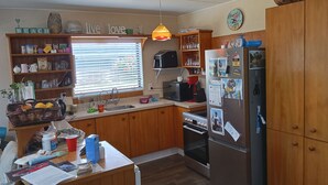 A kitchen with wooden cabinets, a refrigerator, a sink, and various kitchen appliances. - Short walks to Beach & Town. Large deck with BBQ. Super Fast Internet, 85" Tele (Whangamatā)