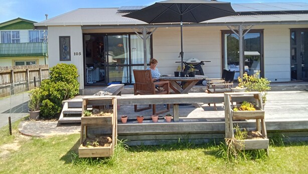 An outdoor patio area with a table and chairs, a large umbrella, and potted plants. - Short walks to Beach & Town. Large deck with BBQ. Super Fast Internet, 85" Tele (Whangamatā)