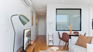 Una sala de estar moderna con televisor de pantalla plana, una lámpara de pie verde, un sofá blanco y un comedor con mesa y sillas.