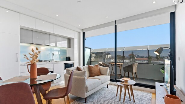 Una sala moderna con sofá, mesa de centro y sillones, una mesa de comedor de vidrio y una cocina al fondo.