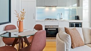 Una cocina moderna con estufa a gas, horno y microondas. Hay una mesa de comedor con sillas y un florero con flores secas. Un sofá con un cojín está en primer plano.