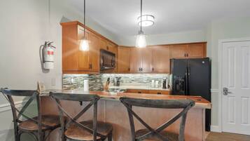 A kitchen with wooden cabinets, a black refrigerator, a coffee maker, and a fire extinguisher. There are three wicker chairs at the island.