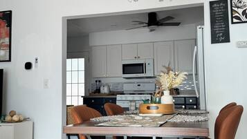 A modern kitchen with white cabinets, a microwave, and a dining area with a wooden table and brown chairs.