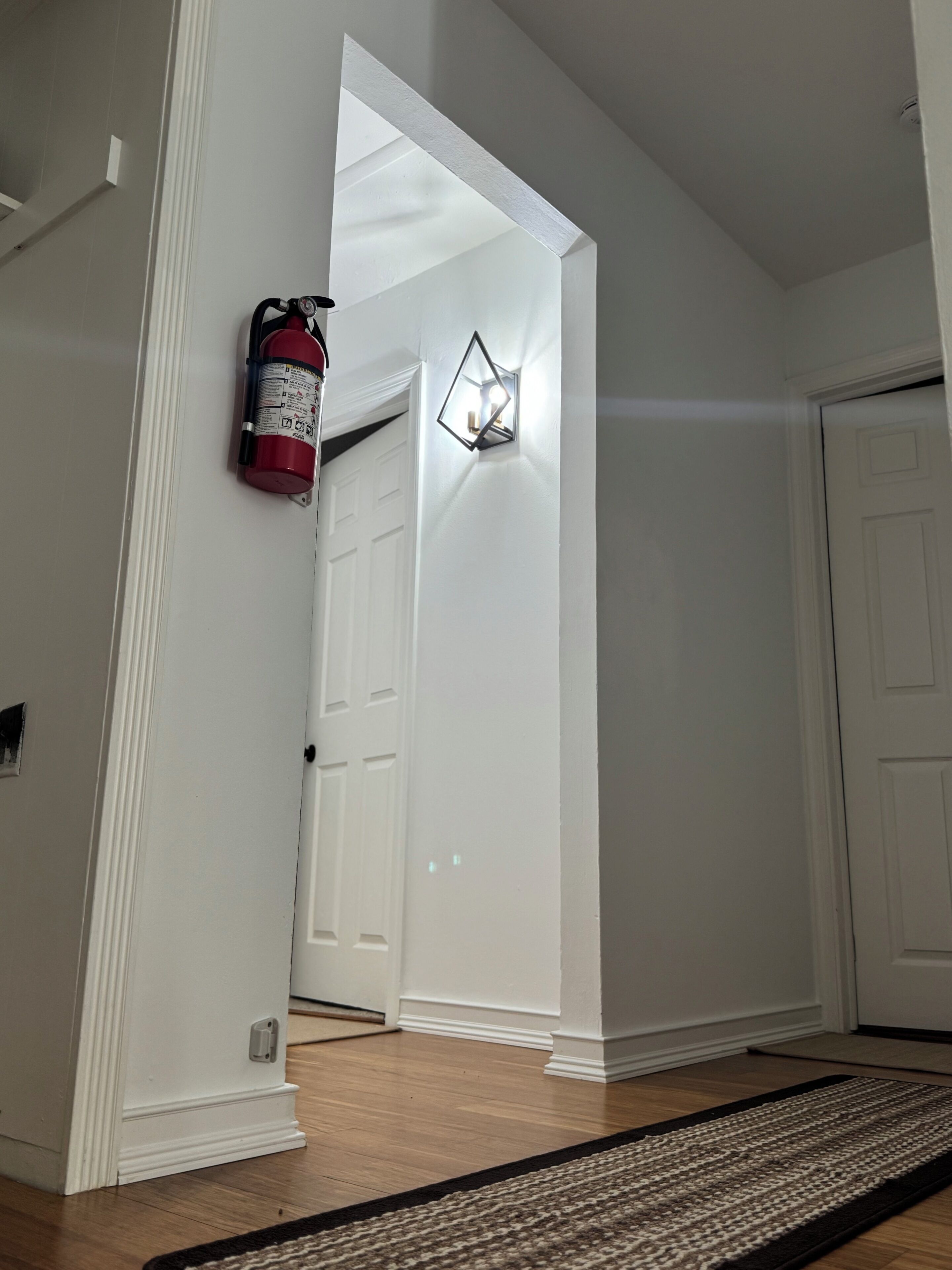 A hallway with a fire extinguisher, a light fixture, and a doormat.