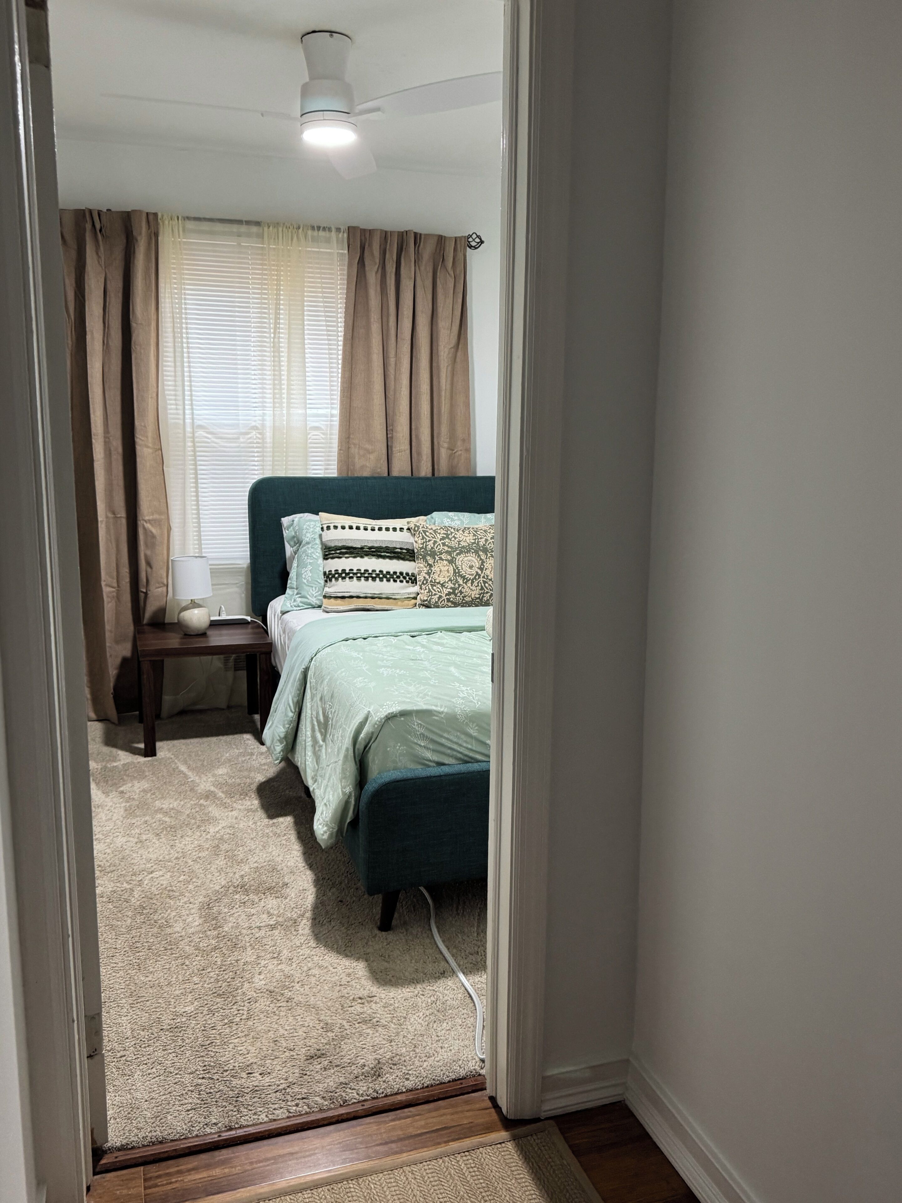 A bedroom with a bed, bedside table, lamp, and a window with curtains.