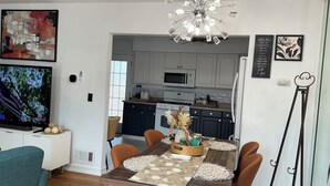 A modern kitchen with white cabinets, a microwave, and a stove. There is a dining area with a wooden table and chairs, and a television in the living room. - South Jersey Shore Comfort & Relaxing  Retreat in Absecon, near  Atlantic City (Absecon)
