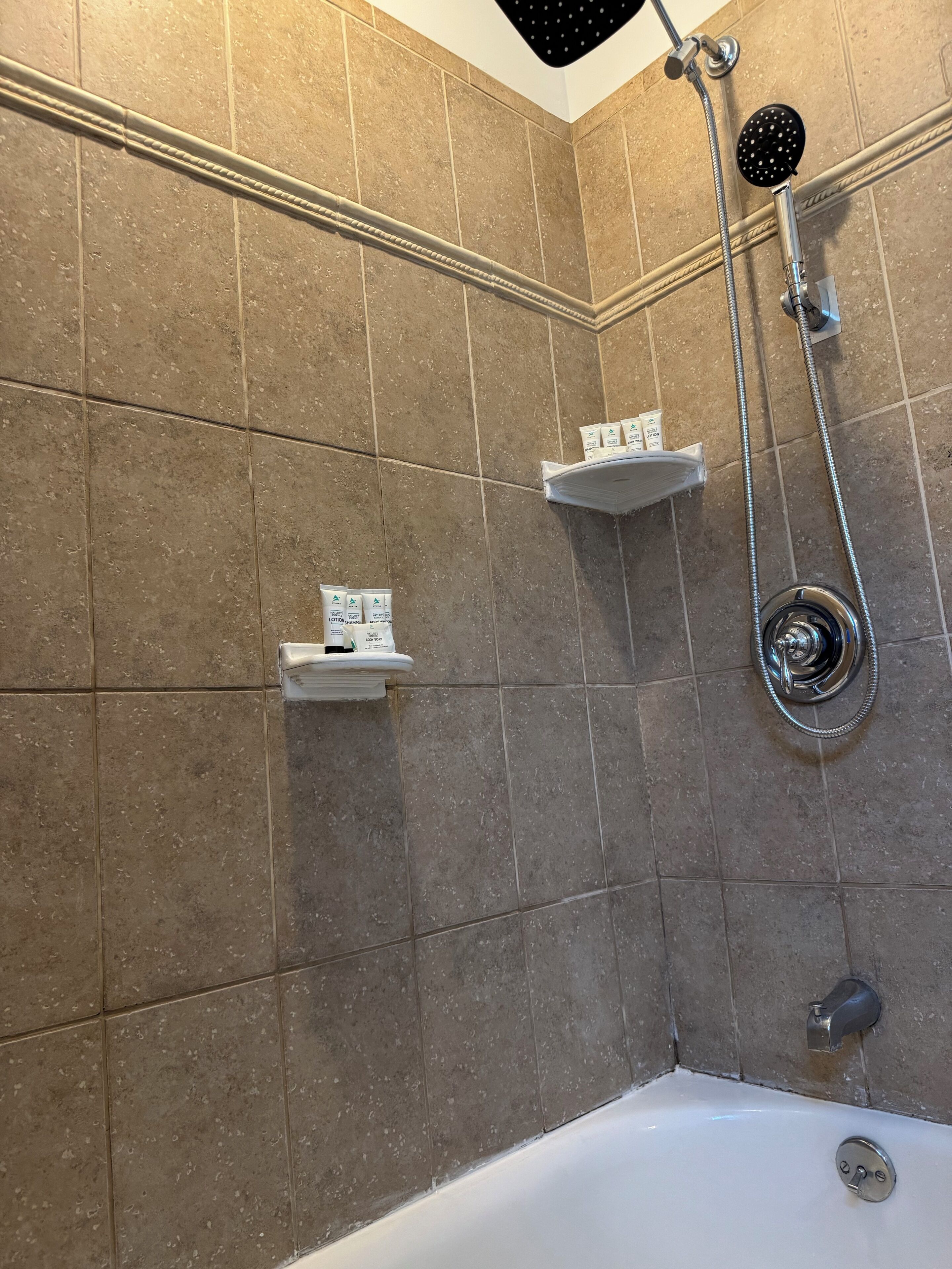 Ein Badezimmer mit einer Badewanne, einer Dusche inklusive Handbrause und zwei kleinen Ablagen für Toilettenartikel.