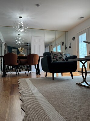Ein modernes Wohnzimmer mit einer Couch, Sesseln, einem Esstisch und einer Chandelüster.