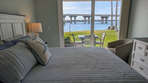 Un dormitorio con cama, mesita de noche, lámpara, cómoda y vista a un puente sobre el agua.