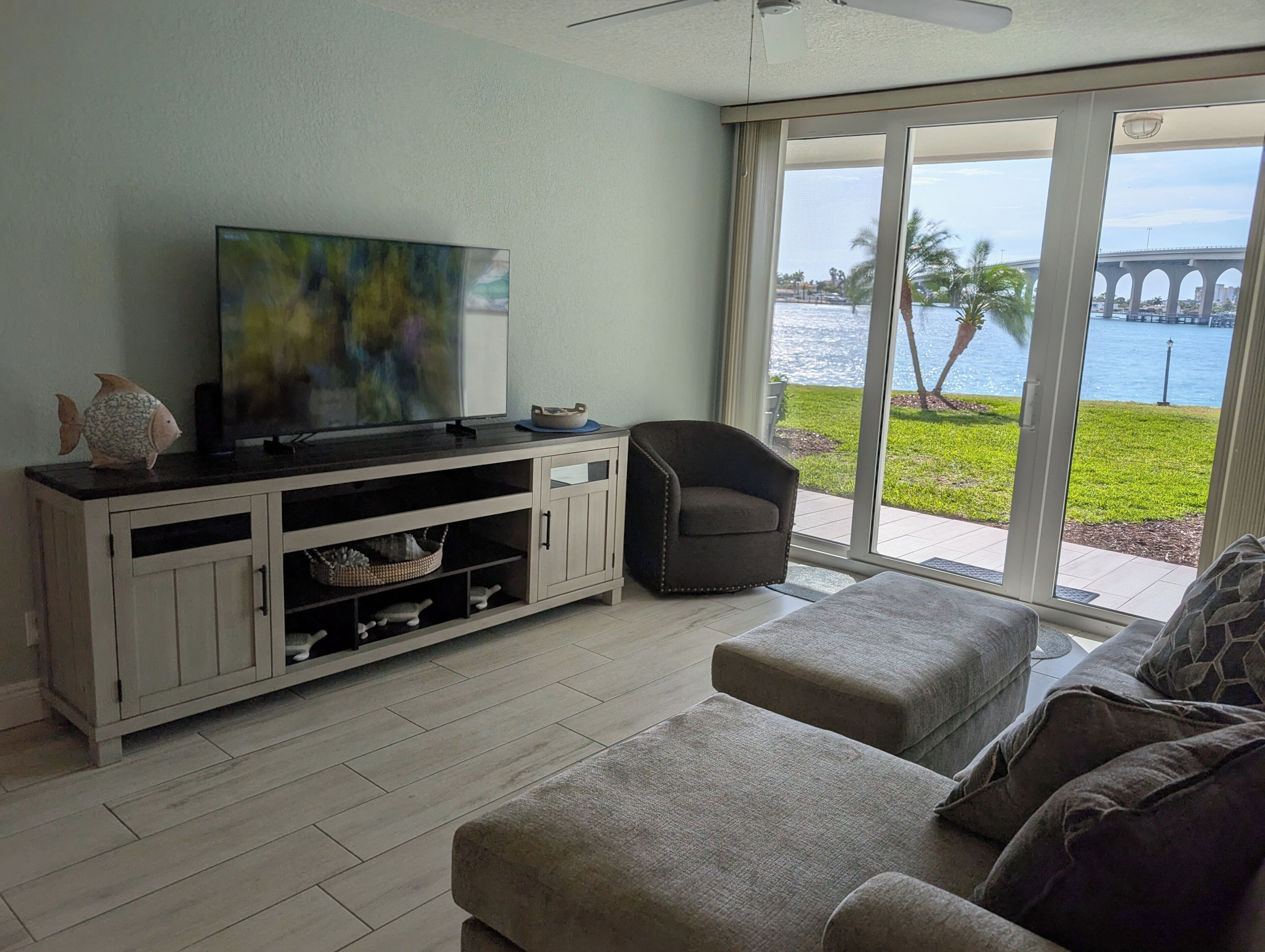 Una sala de estar con televisor, sofá, sillón y vista a un puente y al agua.
