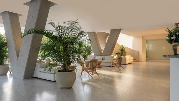 A modern living room with a large potted plant, a white sofa, and a wooden chair. - Apartamento premium a 1 minuto de la playa con todas las comodidades (Magdalena)
