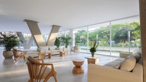 A spacious lobby with a modern design, featuring a large V-shaped architectural element, comfortable seating, and large windows offering a view of the outdoors. - Apartamento premium a 1 minuto de la playa con todas las comodidades (Magdalena)