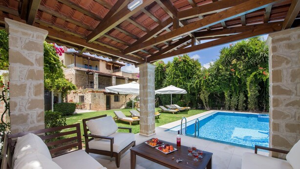 An outdoor patio with a pool, white cushioned seating, and a stone pillar. - Villa for 8 Guests With Gorgeous View (Kissamos)