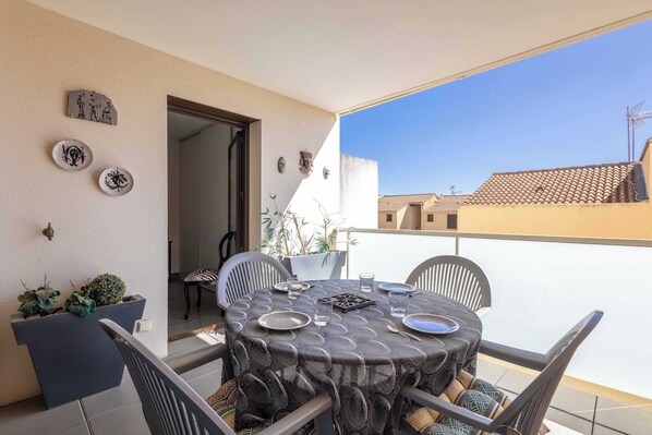 An outdoor dining area with a table set for two, surrounded by chairs, on a balcony with a view of buildings. - Appartement lumineux avec balcon a Valras Plage (Valras-Plage)