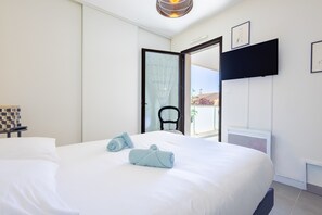 A hotel room with a large bed, a chair, a TV, and a door leading to a balcony. - Appartement lumineux avec balcon a Valras Plage (Valras-Plage)