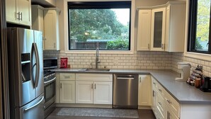 A modern kitchen with white cabinetry, stainless steel appliances, a large window, and a tiled backsplash. - Free driveway parking, fast wifi, peaceful, and private (Oakland)