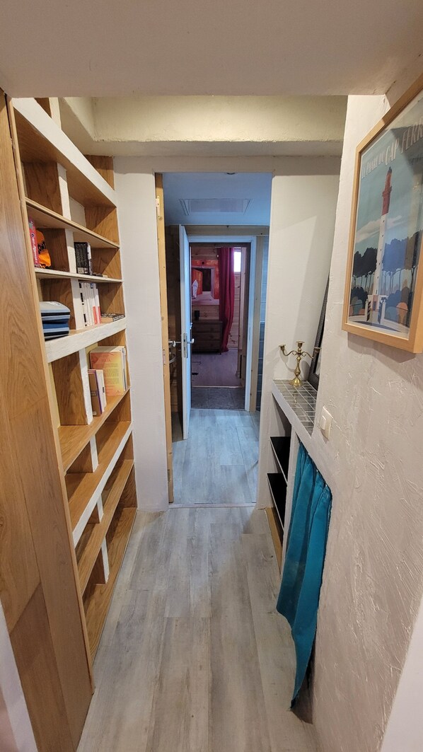 Un pasillo estrecho con estanterías de madera a un lado y una zona de cocina al otro.