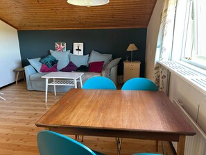 A cozy living room with a wooden ceiling, a sofa with colorful cushions, a small table, and a window with curtains. - 4 Person Holiday Home in Henan (Henån)