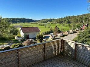 A wooden deck overlooking a rural landscape with a small white building and a red-roofed structure. - 4 Person Holiday Home in Henan (Henån)