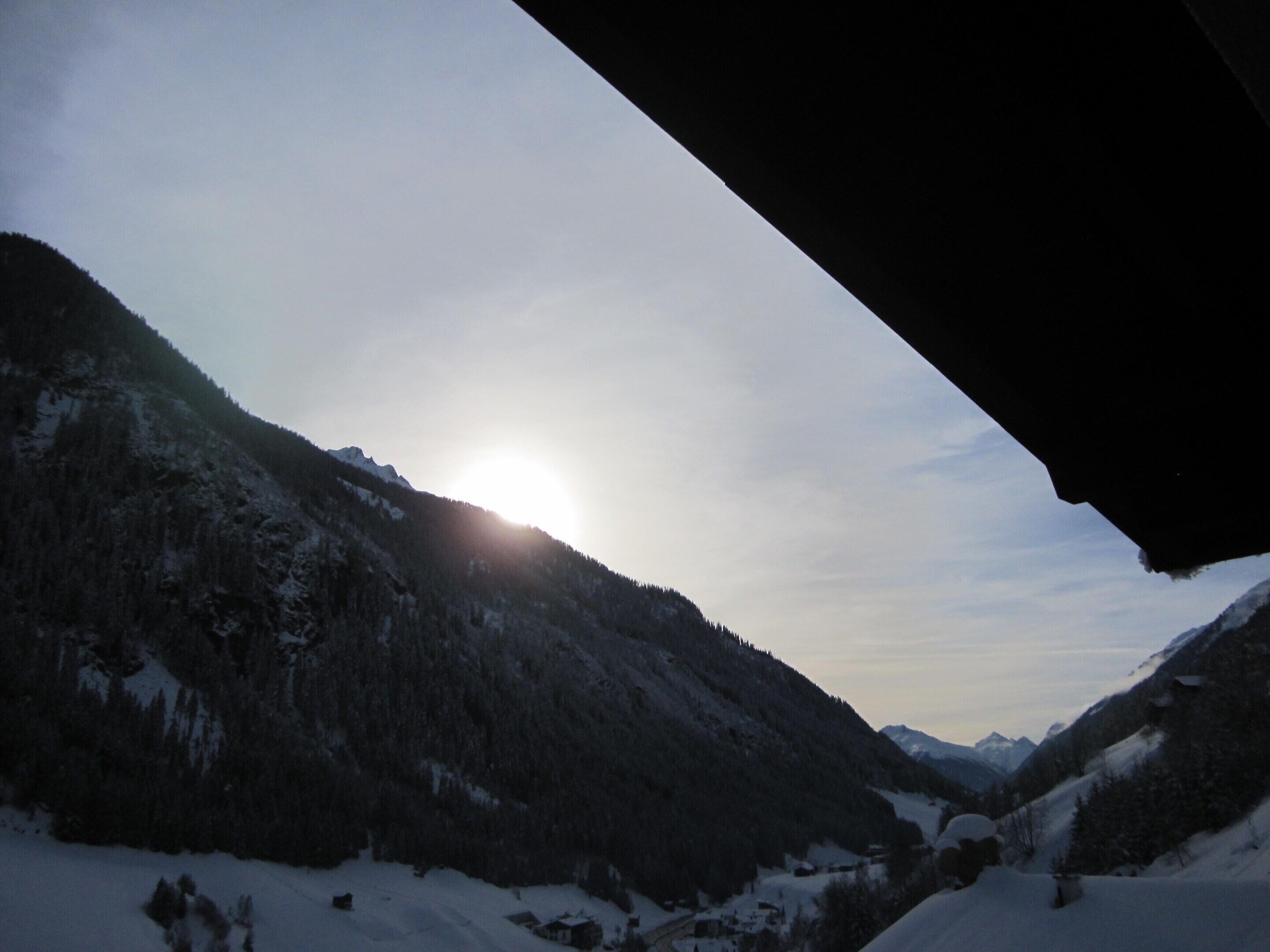 A mountainous landscape with a clear sky and the sun setting or rising.