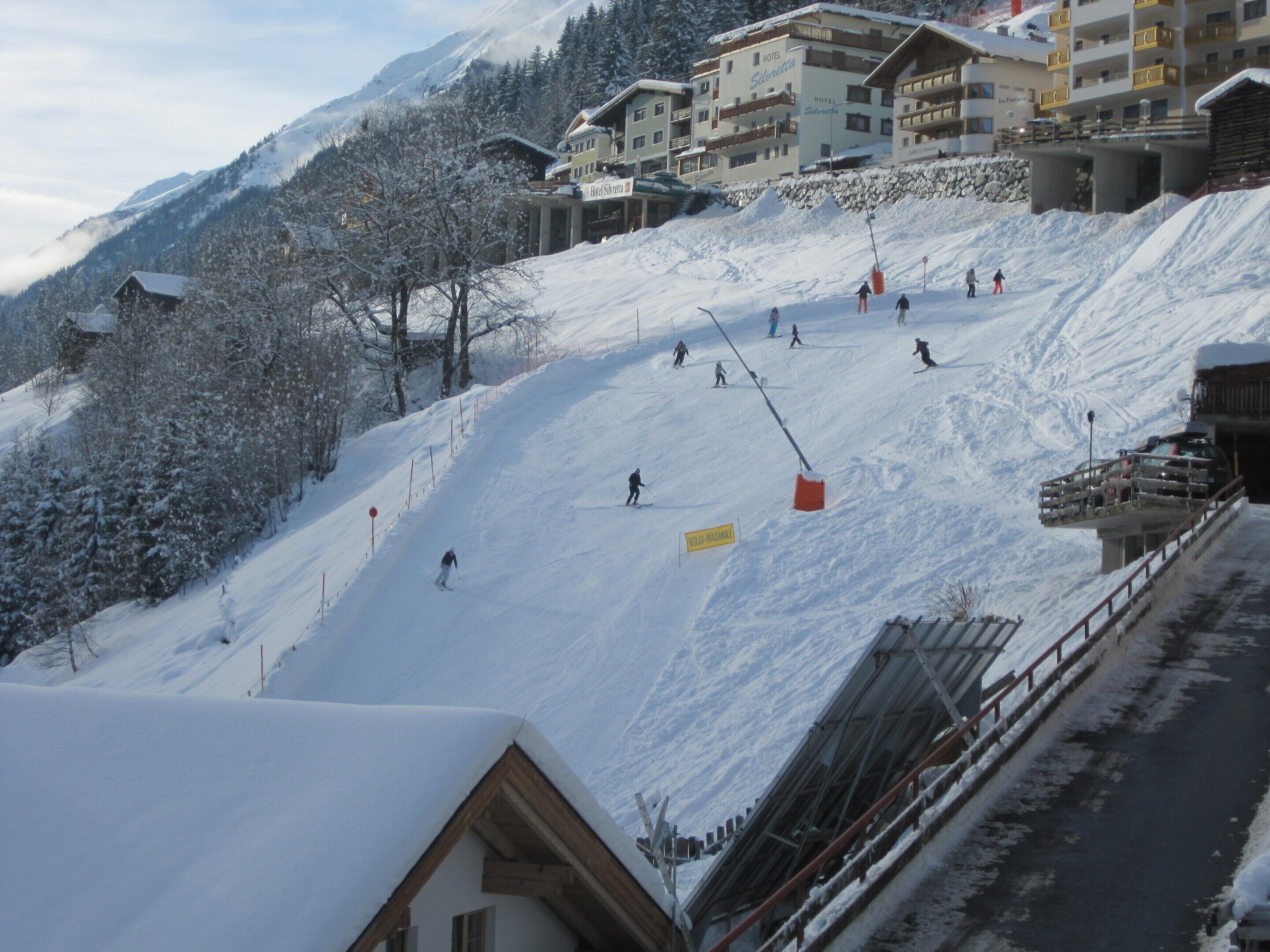 A ski slope with skiers, a hotel named 'Hotel Silvetta' in the background, and a snow-covered mountain.