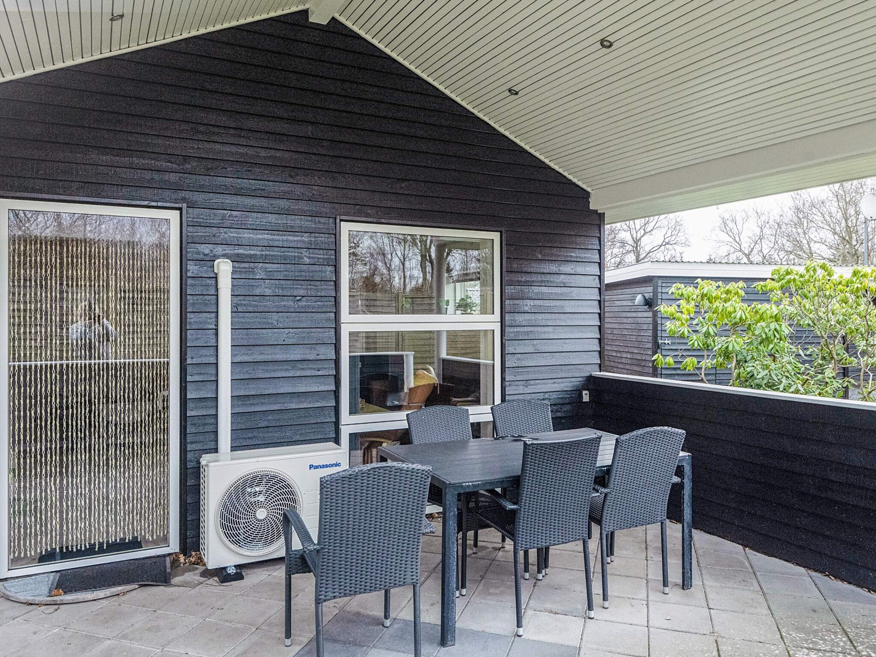 Un patio al aire libre con mesa y sillas, un ventanal grande y un aire acondicionado instalado en la pared.