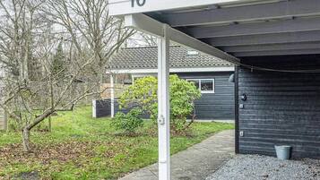 Una propiedad residencial con puerta de garaje, un letrero con el número 10, un camino de entrada pavimentado y un jardín con césped y árboles.