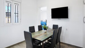 A dining area with a table and chairs, a television on the wall, and a window with blinds. - Welcoming Villa With Private Pool (Conil de la Frontera)