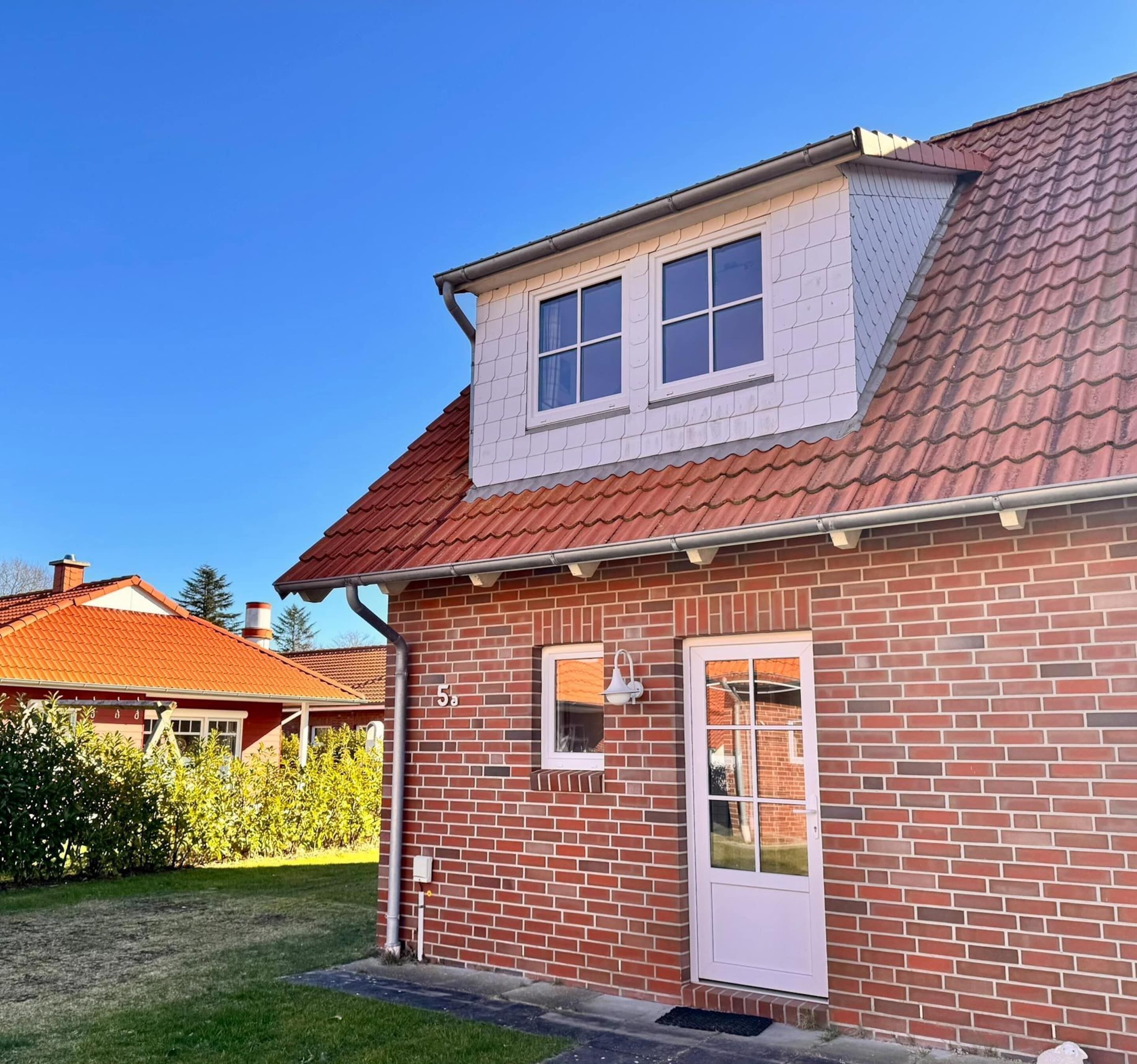 A two-story brick house with a red-tiled roof, a small attic window, and a white door.