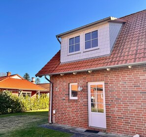 Une maison à deux étages, construite en briques, avec un toit recouvert de tuiles rouges, une petite fenêtre de toit et une porte blanche.