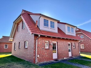 Una casa a due piani in mattoni con tetto rosso, finestre bianche e un piccolo portico.