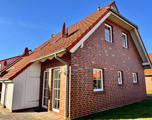 Une maison à deux étages, construite en briques, avec un toit en pente, un garage et un petit abri attenant.