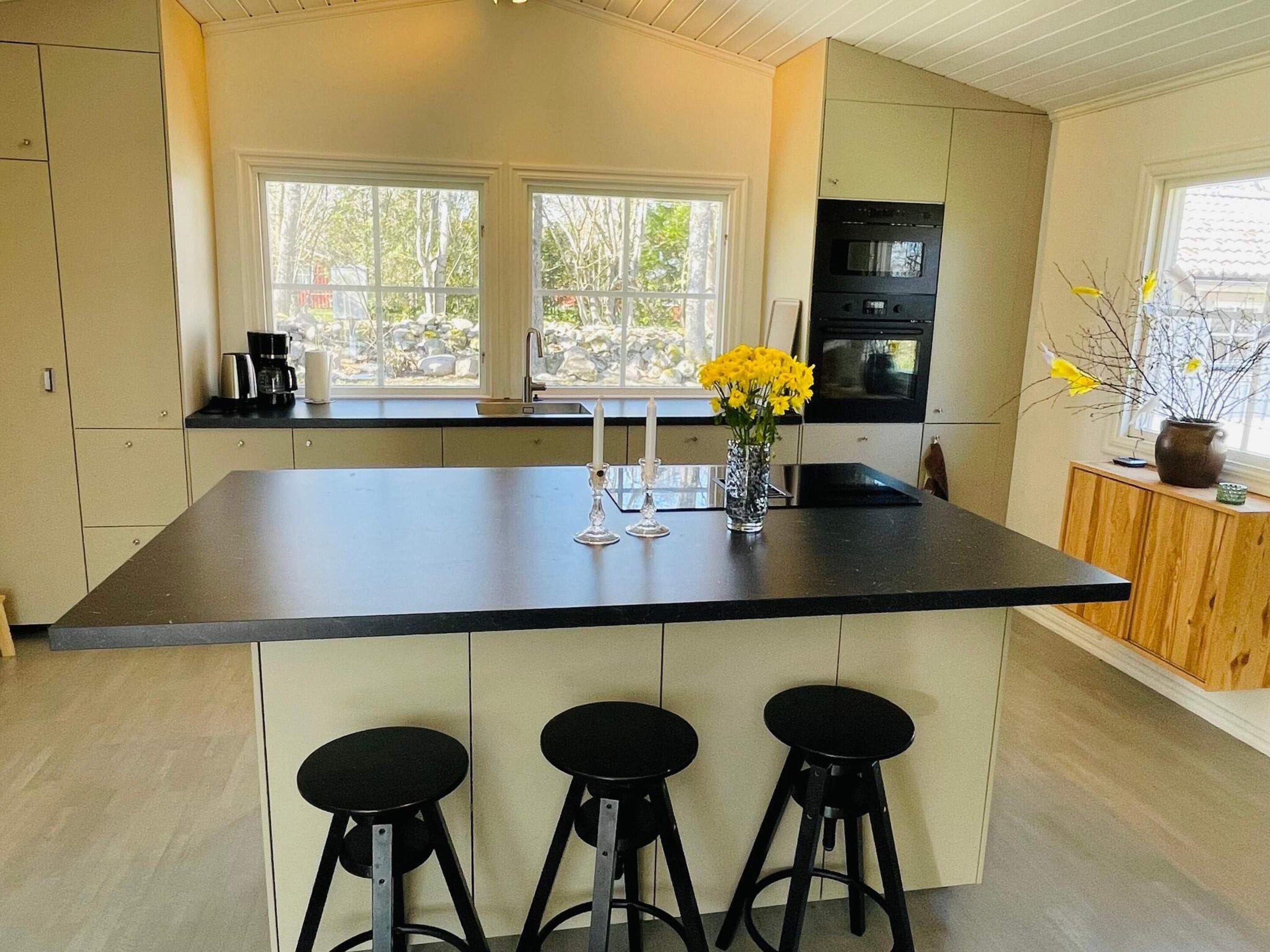A kitchen with a large island, bar stools, a coffee maker, and a vase with yellow flowers.