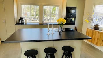 A kitchen with a large island, bar stools, a coffee maker, and a vase with yellow flowers.