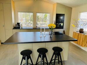 A kitchen with a large island, bar stools, a coffee maker, and a vase with yellow flowers. - 4 Star Holiday Home in Brosarp (Brosarp)