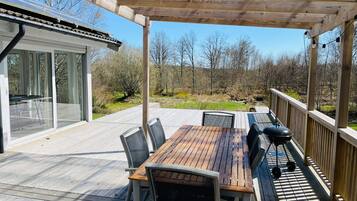 A covered outdoor deck with a wooden table and chairs, a grill, and a glass-enclosed patio area.