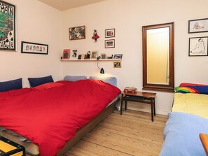 A bedroom with a large bed, a bedside table, a mirror, and various framed pictures on the wall.