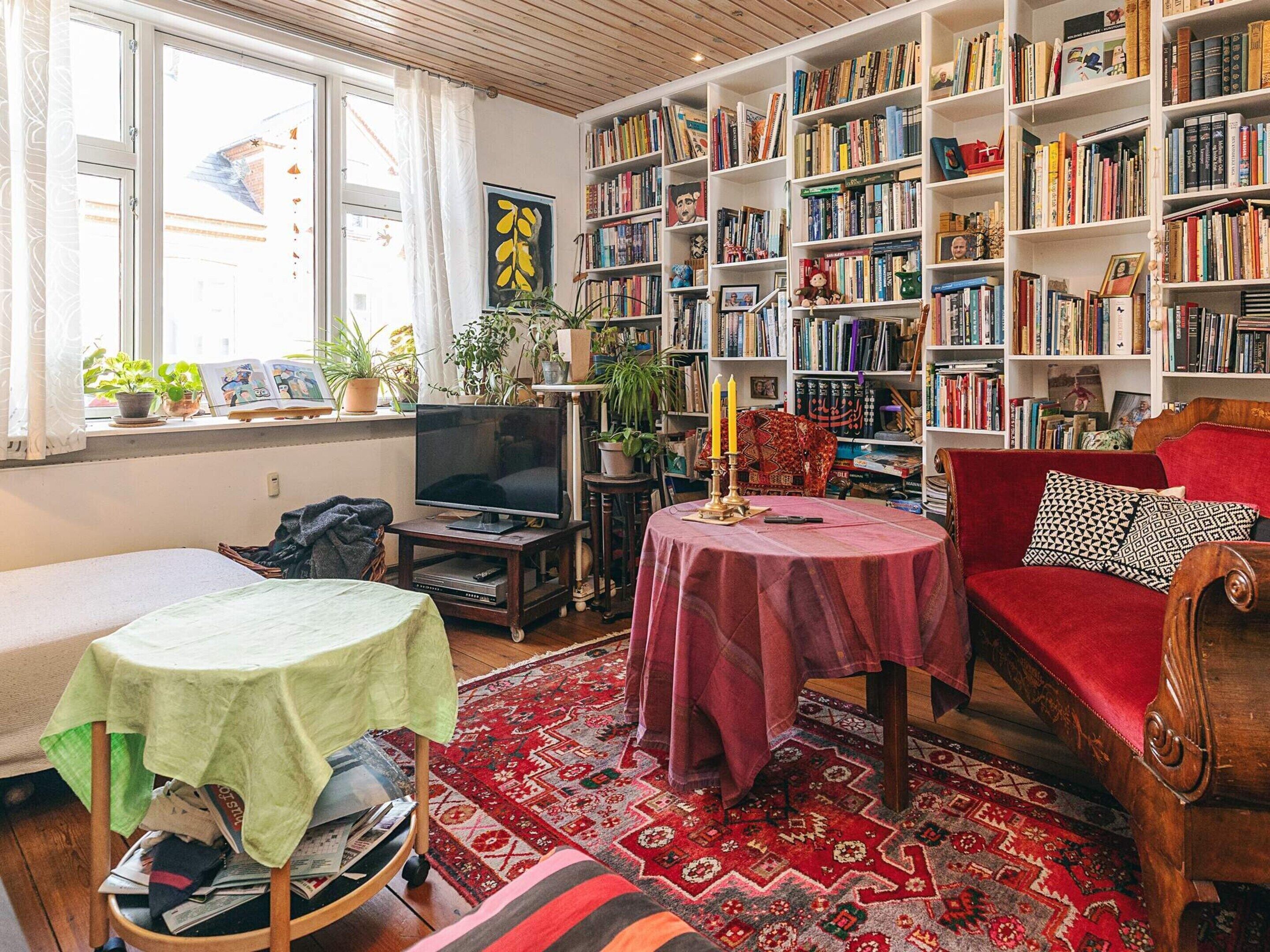 Un salon chaleureux avec une bibliothèque, un téléviseur, un canapé rouge et un tapis à motifs.