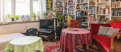 Un salon chaleureux avec une bibliothèque, un téléviseur, un canapé rouge et un tapis à motifs.