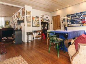 A cozy room with a wooden floor, a dining table with chairs, a bookshelf, and various framed pictures on the walls.