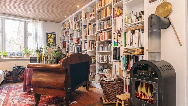 Een gezellige kamer met een houten bank, een open haard, boekenplanken en een raam.